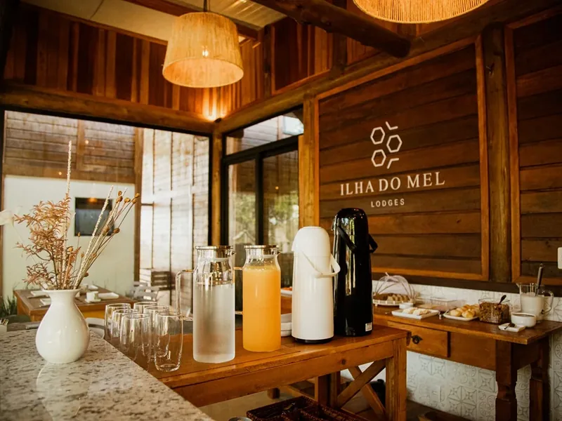 Bancada do café da manhã com sucos, jarras e a logo da pousada na parede de madeira