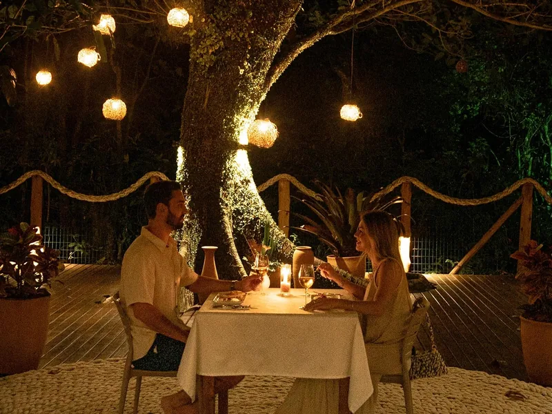 Mesa de jantar para dois sob a figueira iluminada por lanternas, à noite