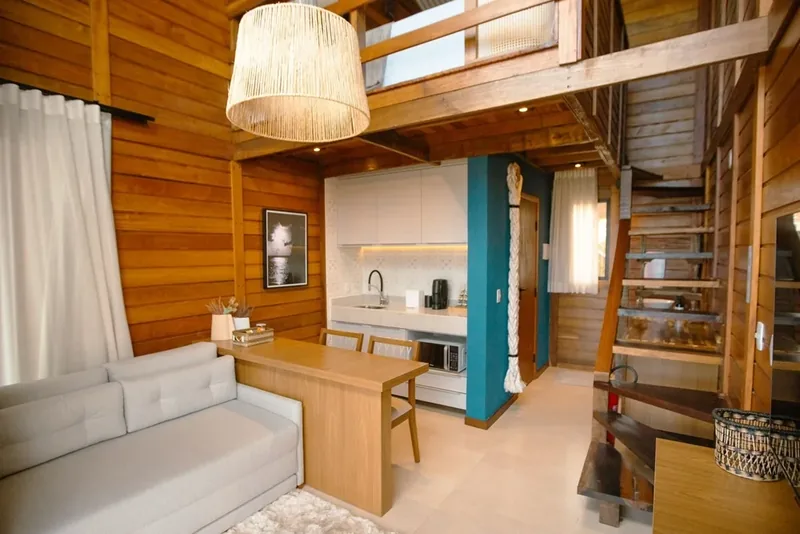 Loft Duplex com sofá, copa e a escada de madeira que sobe ao mezanino