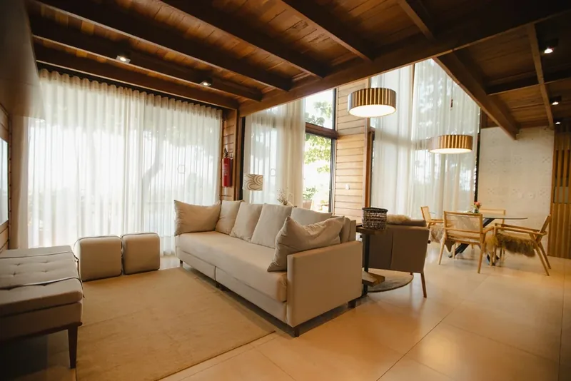 Sala do Lodge Master com sofá claro, mesa de jantar e cortinas abertas para o verde