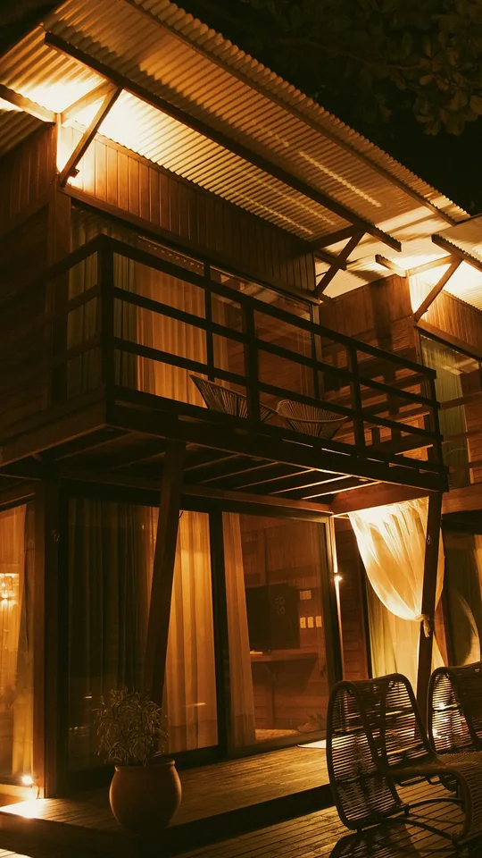 Lodge duplex de madeira iluminado à noite, com varanda e cadeiras no deck