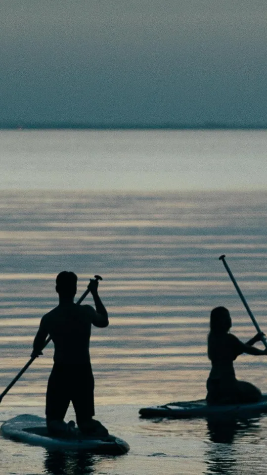 Silhuetas de duas pessoas remando em pranchas de stand up paddle no fim da tarde
